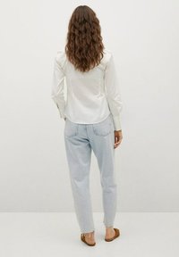 Chemise en satin blanc à manches longues, dos d'un jean bleu clair à coupe décontractée et sandales marron, vue de dos sur un fond neutre.