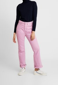 Rosa denimbyxor med avslappnad passform, uppvikta benslut och medelhög midja; kombinerat med en svart långärmad topp och vita sneakers.