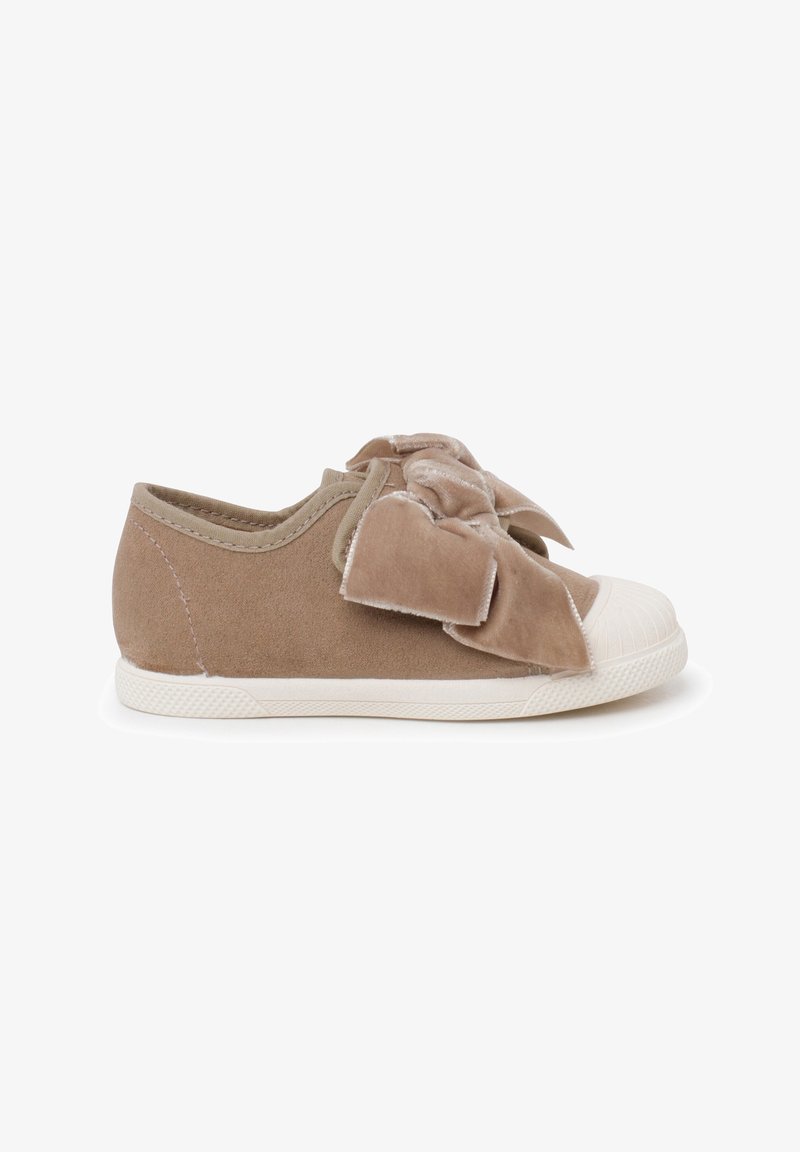 Children's beige suede sneaker with white rubber toe cap and sole, featuring a large soft fabric bow on top.