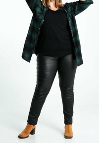 Czarne spodnie z imitacji skóry z pionowymi prążkami, zestawione z czarnym t-shirtem i zieloną koszulą w kratę na guziki. Beżowe botki za kostkę.