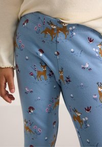 Blå leggings med ett lekfullt mönster av bruna hjortar, blommor och svampar, tillverkade av mjukt tyg med en slät yta.