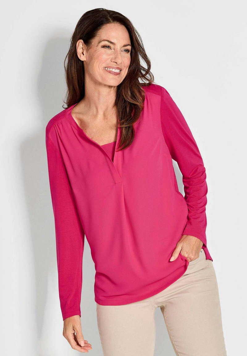 Fuchsie Bluse mit langen  Ärmeln, V-Ausschnitt und lockerer Passform. Aus weichem Stoff mit seitlichen Schlitzen für zusätzlichen Komfort.