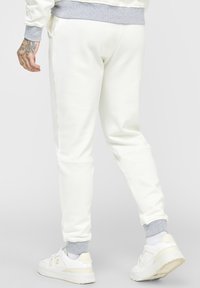 Vita joggingbyxor med grå ribbad midja och mudd vid anklarna, slät textur, avsmalnande ben, sidofickor, parat med vita sneakers.