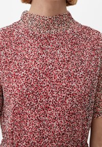 Šaty s květinovým vzorem v odstínech červené a krémové, s vysokým límcem, krátkými rukávy a texturovanou tkaninou se shromážděnými detaily.