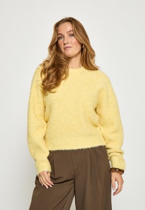Gul, fuzzy sweater med en struktureret overflade, rund halsudskæring og løs pasform, parret med brune højtaljede bukser.