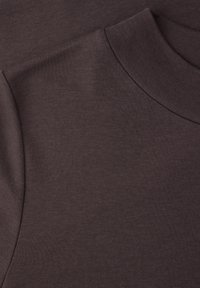 Nærbillede af mørkebrun turtleneck sweater i stof, der viser detaljer omkring kraven og skuldersømmen.