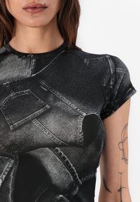 Black short-sleeve t-shirt featuring a denim print, showcasing pockets and seams, with a smooth texture and a fitted design.