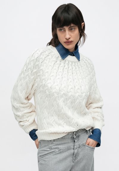 Λευκό πλεκτό πουλόβερ με σχέδιο κοτσίδας, στρογγυλή λαιμόκοψη και κατεβασμένους ώμους, φορεμένο πάνω από μπλε πουκάμισο από ντένιμ, συνδυασμένο με γκρι παντελόνια.