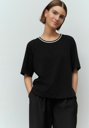 T-shirt noir oversize avec un col rond orné d'une bordure blanche, des manches courtes et une coupe décontractée, associé à un pantalon noir taille haute.