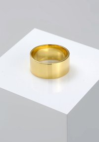 Ein goldfarbener Ring mit einer glatten, polierten Oberfläche, der ein breites Band und ein abgerundetes Innenleben für Komfort aufweist, auf einem weißen Sockel präsentiert.