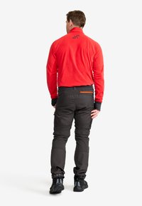 Röd fleecejacka med hög krage, tillsammans med svarta cargobyxor med fickor och elastiska muddar. Svarta vandringsskor fulländar outfiten.