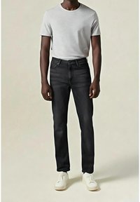 Schwarze Denim-Jeans mit schmaler Passform, ausgestattet mit einem Standardreißverschluss und Taschen, kombiniert mit einem hellgrauen Baumwoll-T-Shirt und weißen Turnschuhen.