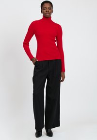 Maglione a collo alto rosso a coste abbinato a pantaloni neri larghi e stivali alla caviglia. Il maglione presenta una silhouette aderente e maniche lunghe.