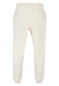 Cremefarvede joggers med en glat tekstur, elastisk talje, sidelommer og ribbede manchetter ved anklerne; simpel, afsmalnet design.