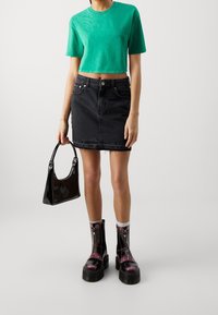 Camiseta verde corta, falda de mezclilla negra con dobladillo deshilachado, bolso negro brillante y botas negras gruesas con acentos rosas y cremalleras.