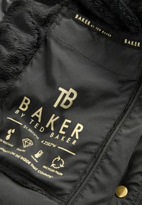 Étiquette en tissu noir avec du texte doré portant "BAKER par Ted Baker." Symboles pour la résistance à l'eau, la durabilité, la chaleur et le remplissage recyclé en dessous.