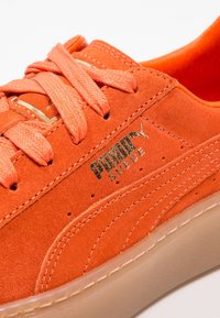 Baskets en daim orange avec surface texturée, lacets plats et branding doré. Comprend une semelle en caoutchouc crème et des détails de couture.