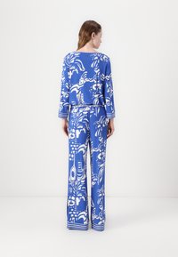 Blauw-wit gestreept loungewear set met lange mouwen en wijde broekspijpen. Bevat een herhalend patroon van tropische motieven en strepen.