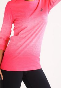 Pitkähiainen urheilupaita, jossa on graadiiniväri vaaleanpunainen, pyöreä pääntie ja hienostunut ribbikuviointi, sekä pieni logo vasemmassa rinnassa.