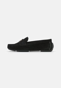 Mocassin loafer en suède noir avec un design cousu, style slip-on et bout rond. Doté d'une semelle extérieure en caoutchouc texturé pour une meilleure adhérence.