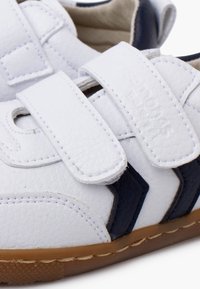 Baskets en cuir blanc avec des accents bleus, dotées de straps velcro, d'une surface texturée et d'une semelle en caoutchouc avec un bord beige.