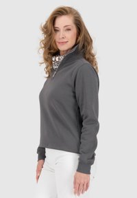 Felpa grigia leggera con zip, colletto alto e rivestimento interno a motivo contrastante. Design aderente, maniche lunghe, polsini a costine.
