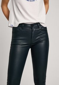 Vaqueros negros de talle alto hechos de un material brillante y liso que cuentan con una cremallera frontal y cierre de botón, con bolsillos laterales y traseros.
