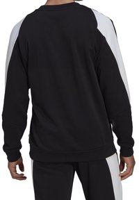 Sweat-shirt noir avec des panneaux latéraux blancs, col rond et manches longues. Présente une coupe décontractée et des poignets côtelés. Texture de tissu douce.