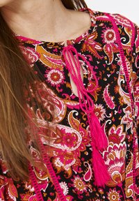 Black fabric top featuring pink and orange paisley patterns, with a keyhole neckline, pink ties, and tassels for decorative accents.