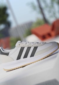 Weißer Sneaker mit schwarzen Streifen und Gummisohle, der auf einer Glasoberfläche im Freien mit verschwommenem Hintergrund liegt.