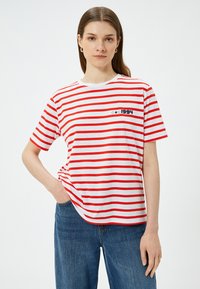 Punainen ja valkoinen raita t-paita pyöreällä kaula-aukolla, vasemmassa rinnassa pieni merensininen printti, jossa lukee "1994" ja tähtiä. Pehmeää puuvillakudosta.