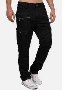 Pantaloni cargo neri con multiple cerniere, tasche frontali e pannelli testurizzati. Realizzati in tessuto resistente; design slim-fit.