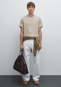 Beige bomulds t-shirt, hvide bukser med vide ben, brunt sweater bundet om taljen, mørkebrun taske og brune slip-on sko. Simpel, minimal design.