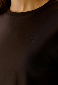 Zwarte t-shirt met korte mouwen, gemaakt van een soepele stof, met een subtiele reliëf hartlogo op de borst en een standaard ronde hals.