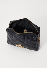 Black quilted leather bag with a gold emblem, zip closure, and fabric lining. Interior features a slip pocket. Textured exterior design.
