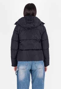 Giubbotto imbottito nero con cappuccio, design trapuntato e vestibilità corta. Abbinato a jeans in denim azzurro chiaro, mostrando uno stile rilassato.
