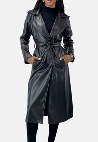 Svart läderrock med bälte i midjan, stora slag, dubbelknäppning och två sidofickor. Mjuk textur med knälång längd.