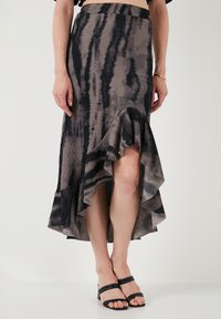 Falda midi asimétrica en gris apagado con patrón abstracto negro, con un dobladillo con volantes y tejido ligero. Llevada con sandalias negras de tiras.