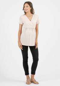 Jasnoróżowa bluzka z krótkim rękawem o kroju kopertowym i marszczonym pasie, zestawiona z czarnymi dopasowanymi spodniami i srebrnymi płaskimi sandałami.