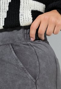 Grå sweatpants med tekstureret finish, der har sidelommer og elastisk talje. Den øverste del viser en sort og hvid strikket sweater.