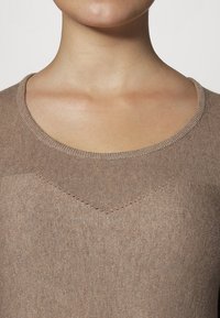 Maglione lavorato a maglia beige con scollatura rotonda e un sottile dettaglio a V sul petto, caratterizzato da una texture liscia e un tessuto leggero.