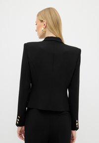 Blazer nero con spalle strutturate e una vestibilità su misura, caratterizzato da bottoni dorati sulle maniche e una texture di tessuto liscia.