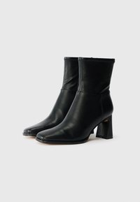 Black leather ankle boots with a fitted design, square toe, and a chunky, geometric heel. Smooth texture with minimal stitching details.
