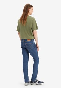 Olivengrønn avkortet t-skjorte kombinert med blå denimjeans. Slitt tekstur på jeansene, gummisåle sneakers i marineblått med hvite detaljer.