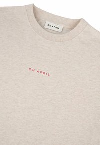 Šviesiai smėlinis apvalios iškirpės marškinėliai su subtilia tekstūra. Ant kairiojo šono yra mažas rožinis „OH APRIL“ logotipas. Minkšta medvilnė.