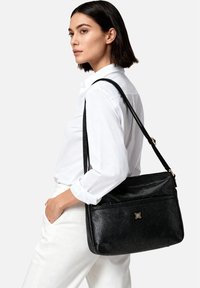 Borsa in pelle nera granulata con tracolla regolabile, dettagli in metallo dorato, tasca frontale con zip, forma rettangolare e superficie texturizzata.