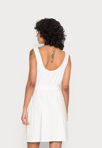 Vestido branco sem mangas com costas em V, cintura ajustada e saia rodada. Feito de tecido suave, apresentando uma textura lisa e um design simples.