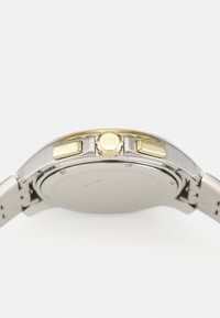 Montre en argent et en or avec un bracelet en métal, boîtier rond, couronne proéminente et deux boutons-poussoirs. Texture lisse et finition polie.