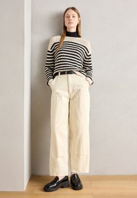 Stripete strikkegenser i beige og svart, kombinert med høy Midje kremfargede bukser. Svart skinn loafers fullfører antrekket.