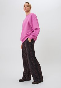 Felpa rosa oversized con polsini a costine, abbinata a pantaloni neri larghi con un motivo di stampa leopardo marrone.